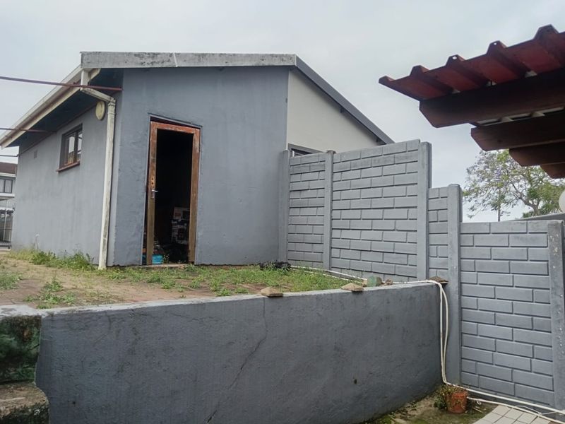 Rear exterior view of the property featuring a painted masonry structure, precast concrete boundary wall, and paved patio area requiring maintenance.