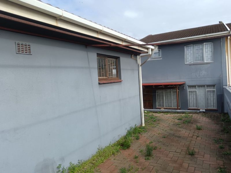 Rear exterior view of the property featuring paved courtyard area, security bars on windows, and guttering system requiring maintenance.