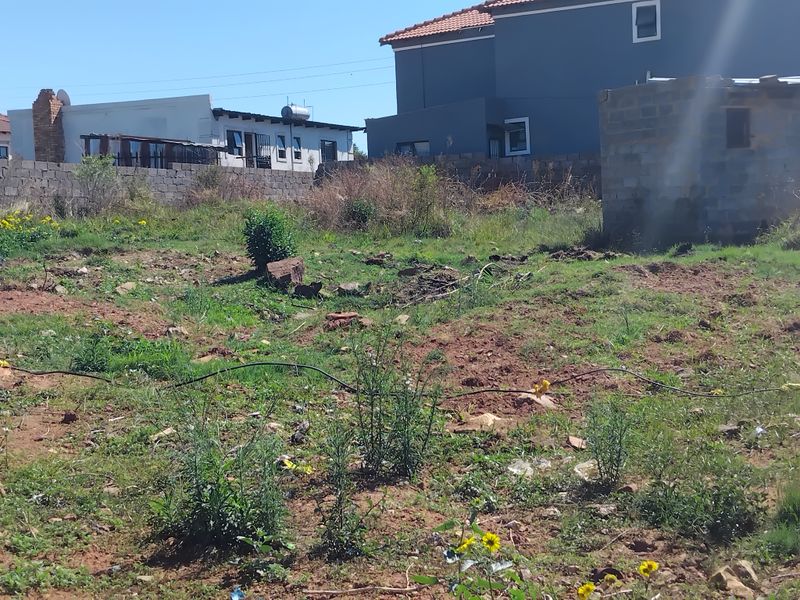 An undeveloped plot of land featuring uneven terrain, wild vegetation, and a partial masonry structure, enclosed by a perimeter wall.