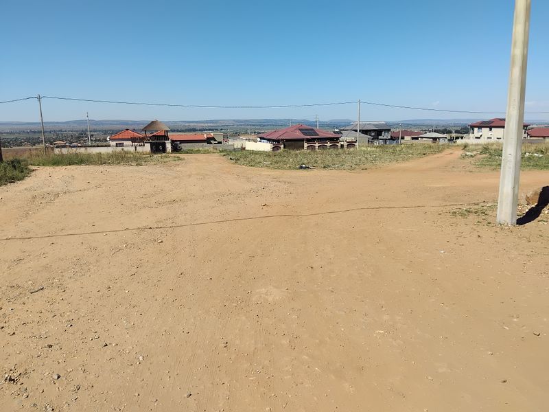 A view of an unpaved road and utility infrastructure in a residential area with surrounding houses in the distance.