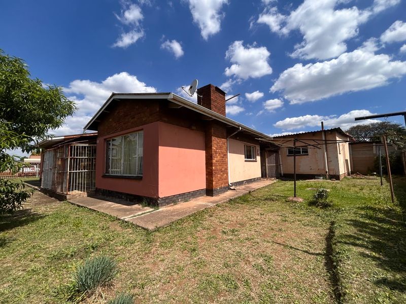 Rear view of the property featuring a brick chimney, concrete patio area, and established garden space with security gates.