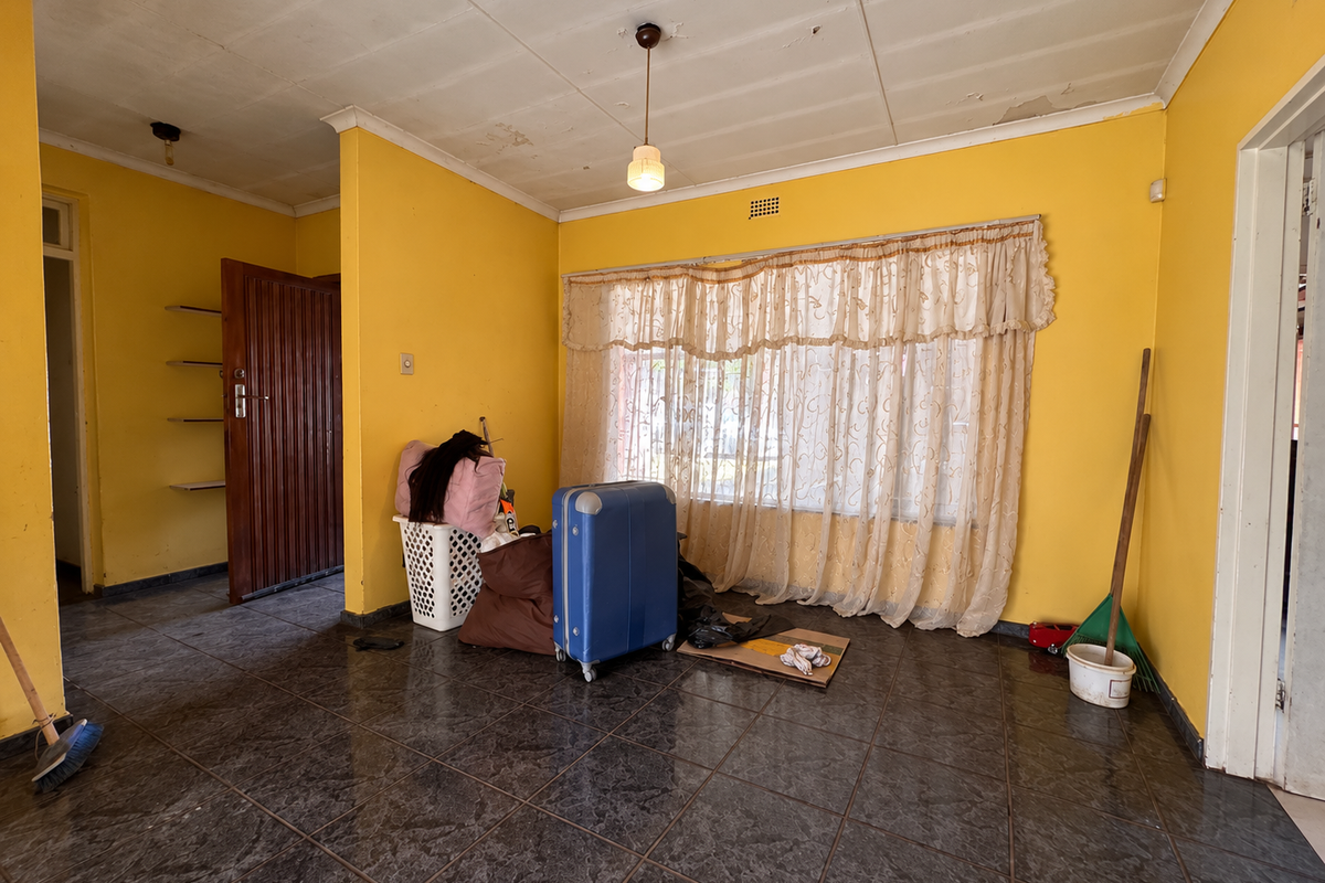 A living room featuring dark tiled flooring, yellow walls, and built-in shelving, requiring cosmetic updates to the ceiling and wall finishes.