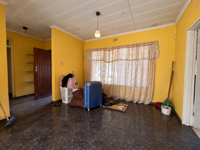 A living room featuring dark tiled flooring, yellow walls, and built-in shelving, requiring cosmetic updates to the ceiling and wall finishes.