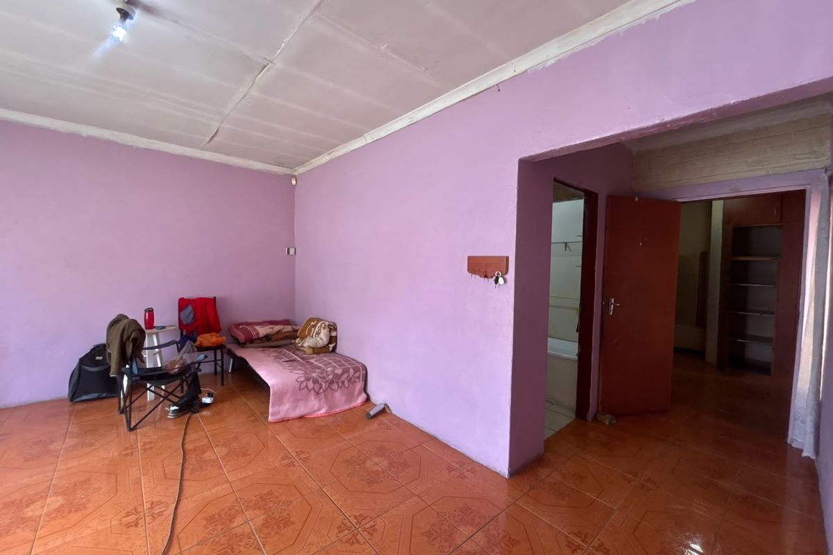 A bedroom featuring tiled flooring and access to an adjoining room, requiring cosmetic updates to the walls and ceiling to improve its overall condition.