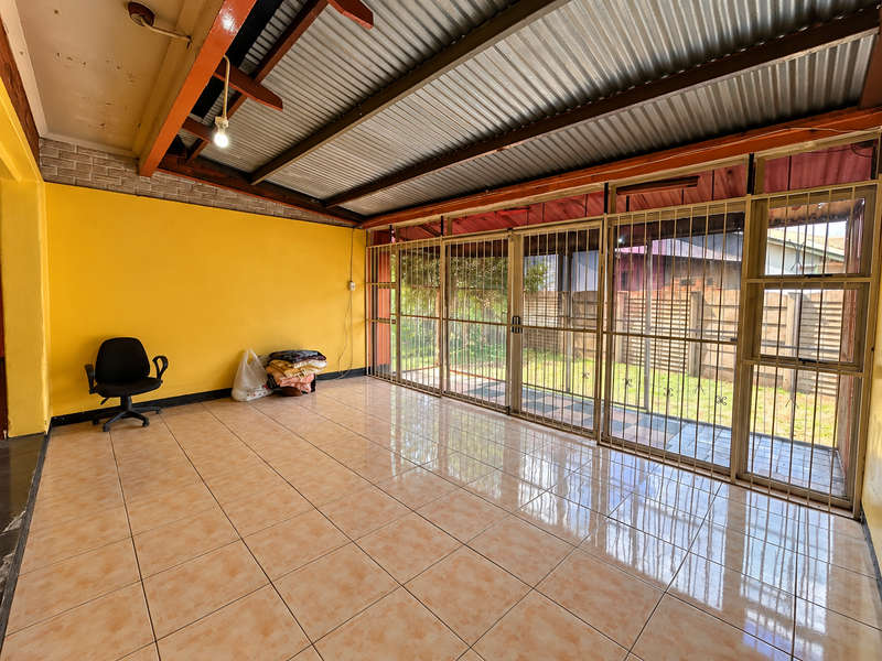 A spacious covered patio featuring tiled flooring, exposed timber beams, and large security-gated glass doors opening to the garden.
