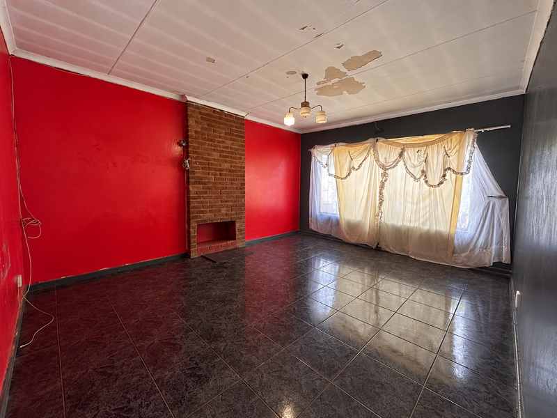 Spacious living room featuring a brick fireplace, dark tiled flooring, and significant ceiling damage requiring repair and cosmetic updates.