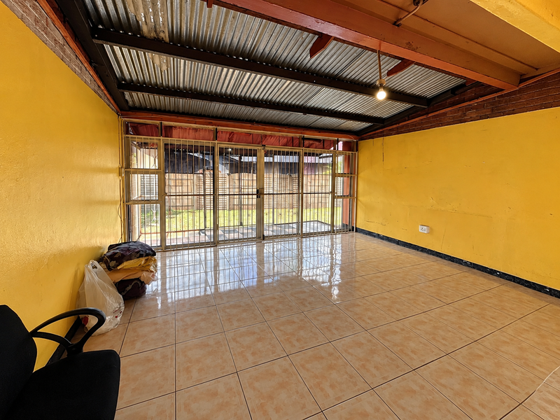 An enclosed patio area featuring tiled flooring, exposed timber beams, and a corrugated metal roof, secured with metal security gates.