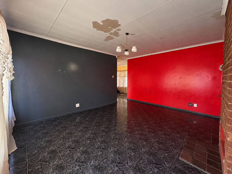 An empty living room featuring dark tiled flooring, a brick fireplace, and bold accent walls, requiring ceiling and wall maintenance.