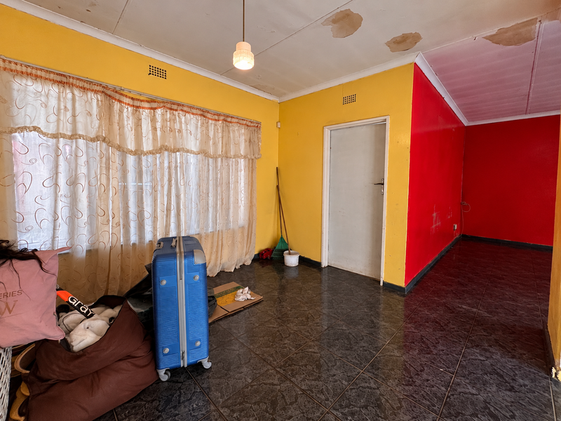 A vacant living area featuring dark tiled flooring, bright yellow and red walls, and visible ceiling water damage requiring maintenance.