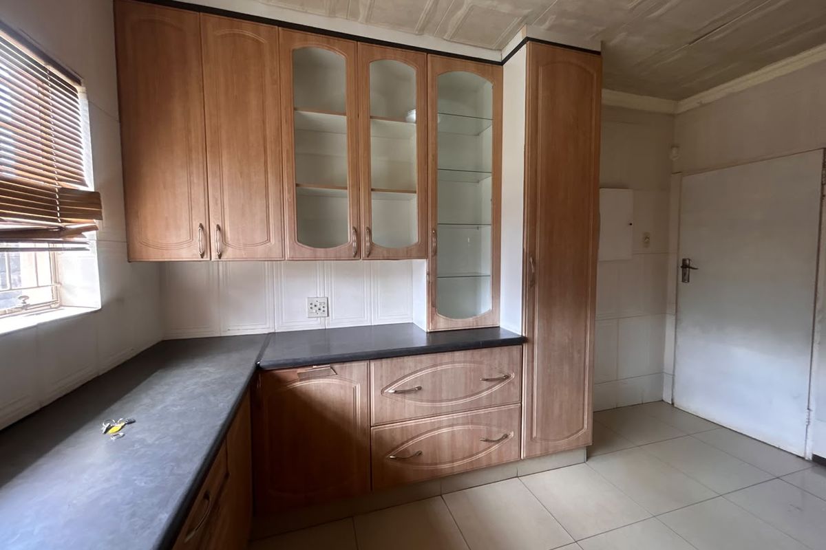 A functional kitchen featuring wood-look laminate cabinetry, glass display units, dark countertops, and tiled flooring, offering a clean space ready for modern updates.