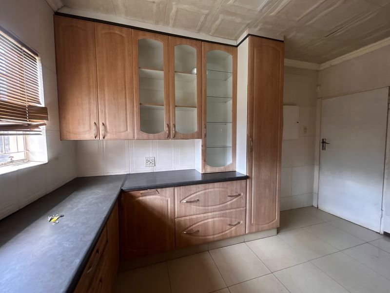 A functional kitchen featuring wood-look laminate cabinetry, glass display units, dark countertops, and tiled flooring, offering a clean space ready for modern updates.