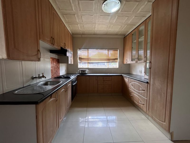 A functional kitchen featuring extensive wooden cabinetry, laminate countertops, built-in oven and hob, and tiled flooring, offering a classic layout ready for modernization.