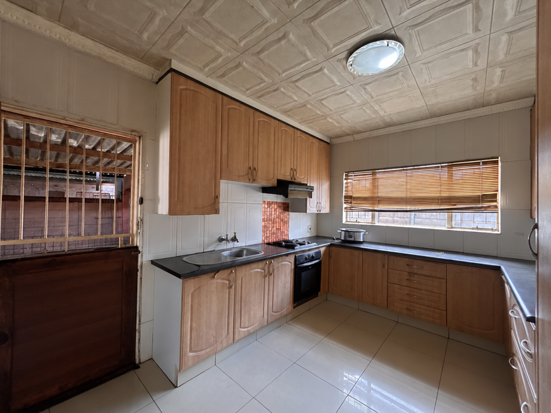 A functional kitchen featuring wooden cabinetry, laminate countertops, built-in oven, and hob, with tiled flooring and a secure entrance door.
