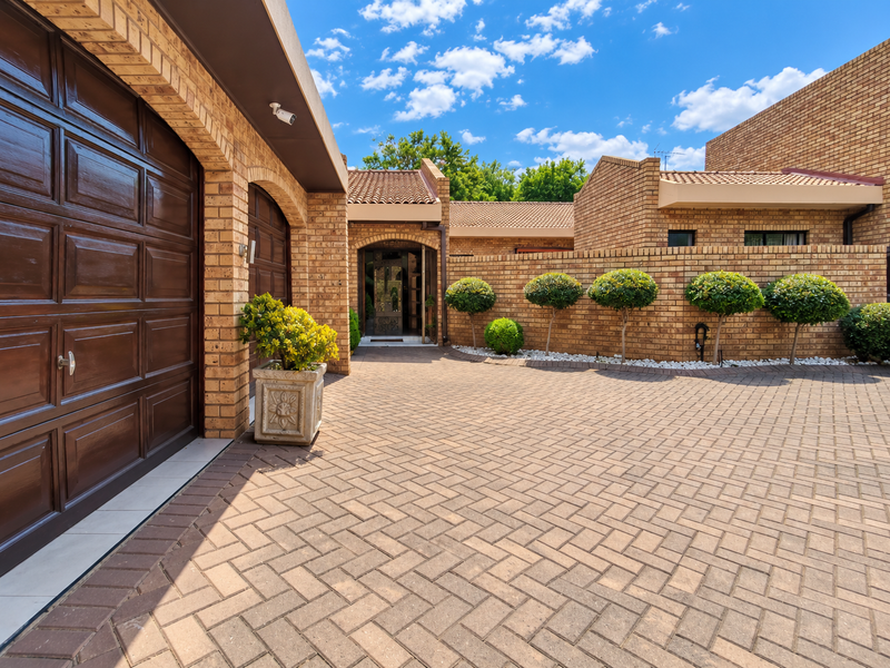 A well-maintained townhouse exterior featuring a paved driveway, double garage, and neat brick facade with established landscaping.