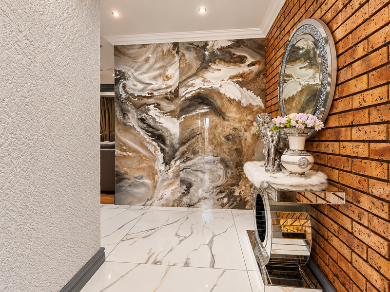 A modern, well-lit hallway featuring a striking marble-effect feature wall, polished marble-look floor tiles, and a contrasting exposed brick wall.