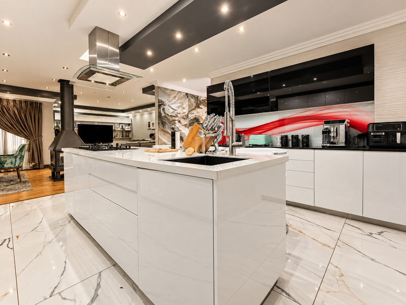 Modern open-plan kitchen featuring a central island with quartz countertops, high-gloss cabinetry, integrated appliances, and elegant marble-look flooring, seamlessly flowing into the living area.