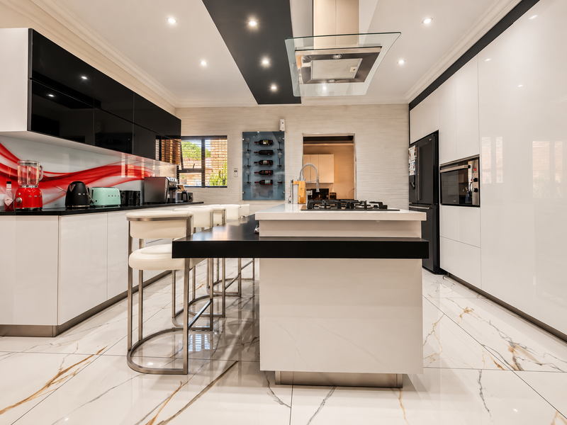 Modern, high-end kitchen featuring a central island with gas cooktop, sleek cabinetry, integrated appliances, and polished marble-look flooring.