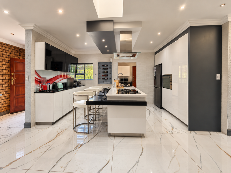 Modern, high-end kitchen featuring a central island with gas cooktop, sleek cabinetry, integrated appliances, and polished marble-look floor tiles.