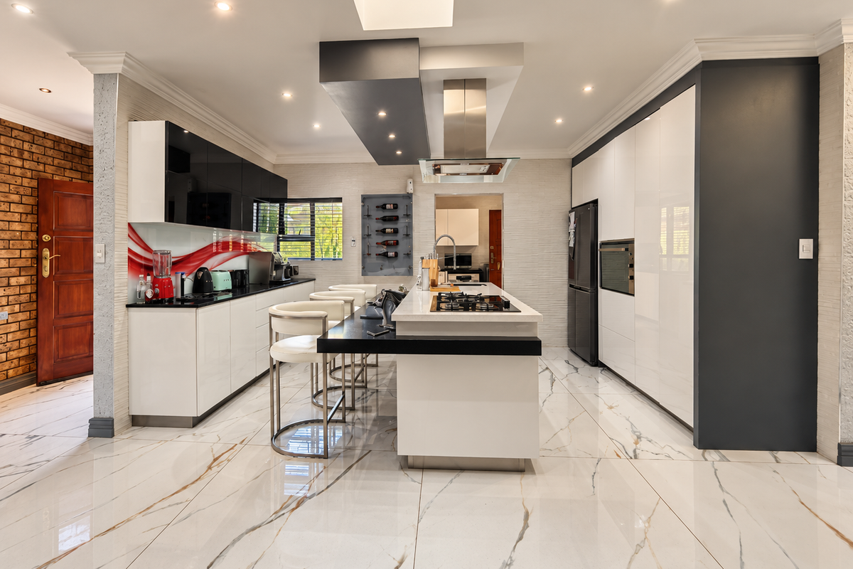 Modern, high-end kitchen featuring a central island with gas cooktop, sleek cabinetry, integrated appliances, and polished marble-look floor tiles.