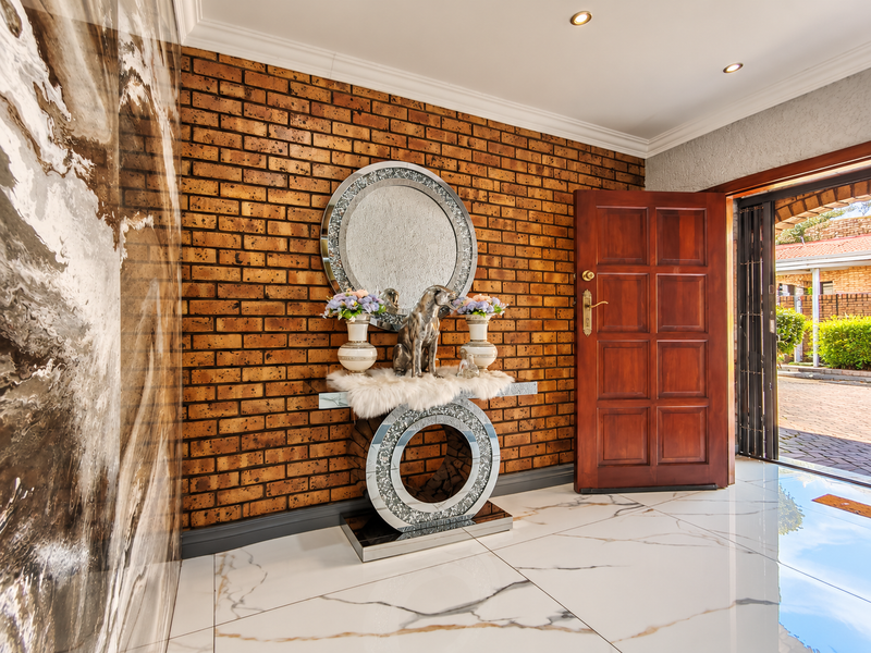 Welcoming entrance hall featuring a striking exposed brick feature wall, polished marble-look porcelain floor tiles, and a solid timber front door.