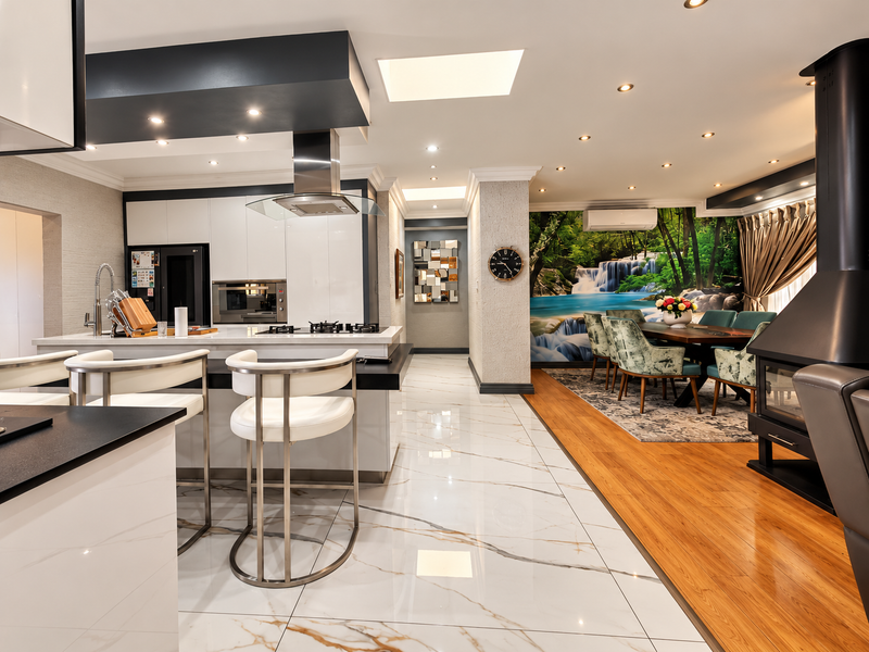 Spacious open-plan living and kitchen area featuring a modern kitchen island, built-in appliances, fireplace, and a blend of marble-look and hardwood flooring.