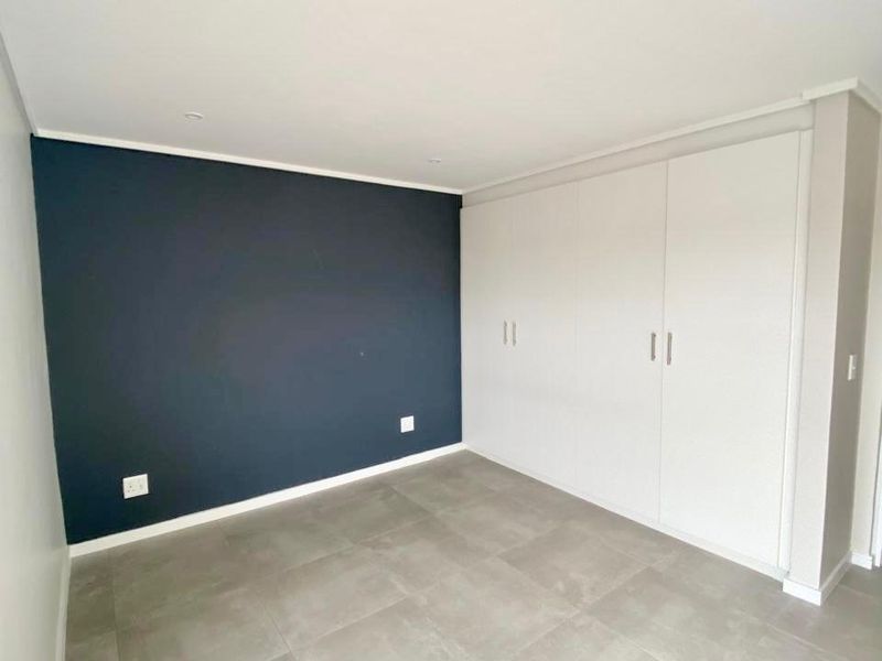 A clean, empty bedroom featuring neutral tiled flooring, a dark accent wall, and ample built-in cupboard storage.