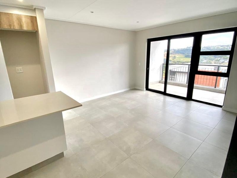 A bright, modern open-plan living area featuring large format floor tiles, a stone kitchen island, and sliding glass doors leading to a balcony.