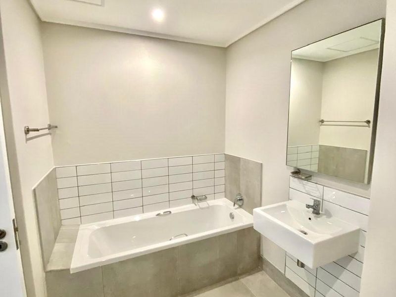 Modern bathroom featuring a built-in bathtub, wall-mounted basin, and neutral tiled finishes, presenting a clean and well-maintained space.