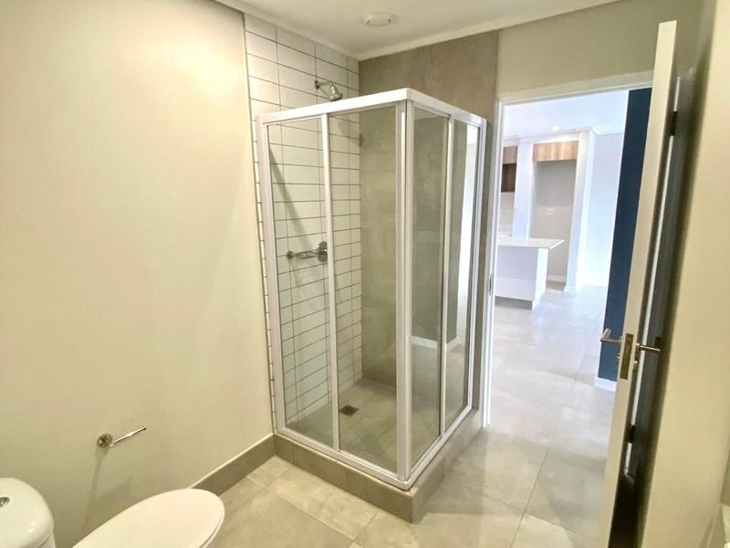 A clean, modern bathroom featuring a glass-enclosed shower, neutral floor tiles, and contemporary fixtures, presenting a well-maintained and functional space.