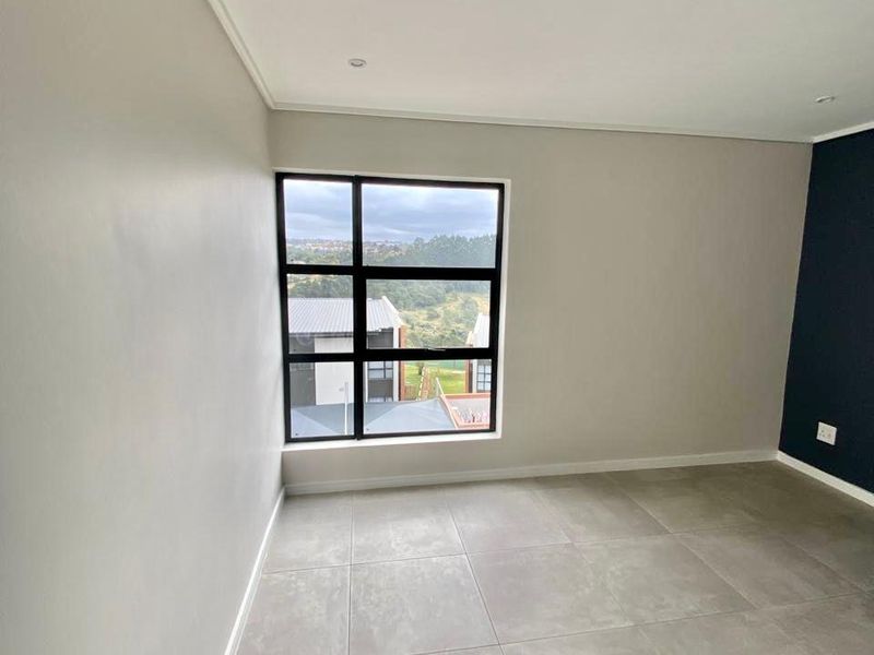 A bright, empty bedroom featuring large format floor tiles, a modern black-framed window, and a dark accent wall, offering a clean and neutral canvas.