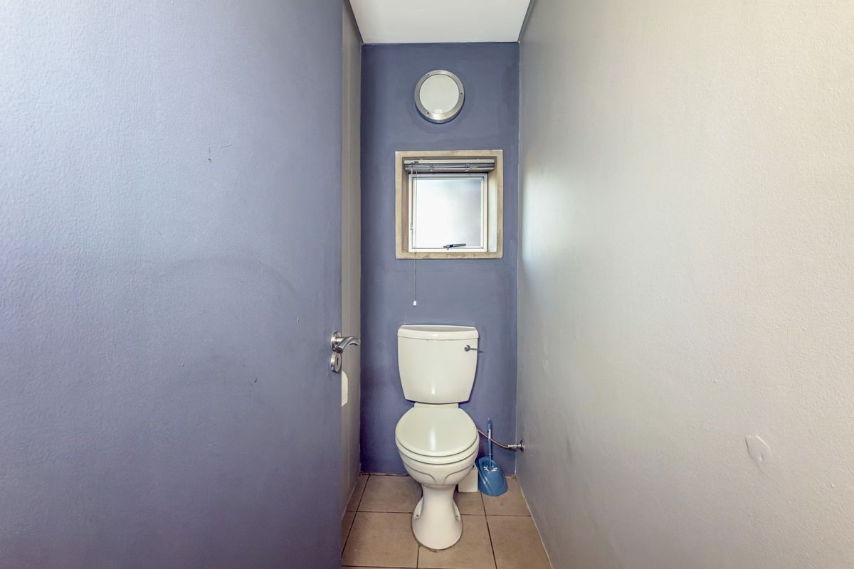 A compact guest toilet featuring tiled flooring, a window for ventilation, and a simple wall-mounted light fixture.