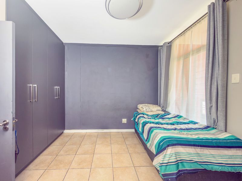 A bedroom featuring tiled flooring, built-in cupboards, and a large window with curtains, providing natural light.