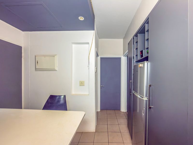 A functional kitchen area featuring built-in cabinetry, tiled flooring, and recessed lighting, currently showing signs of wear and exposed wiring.