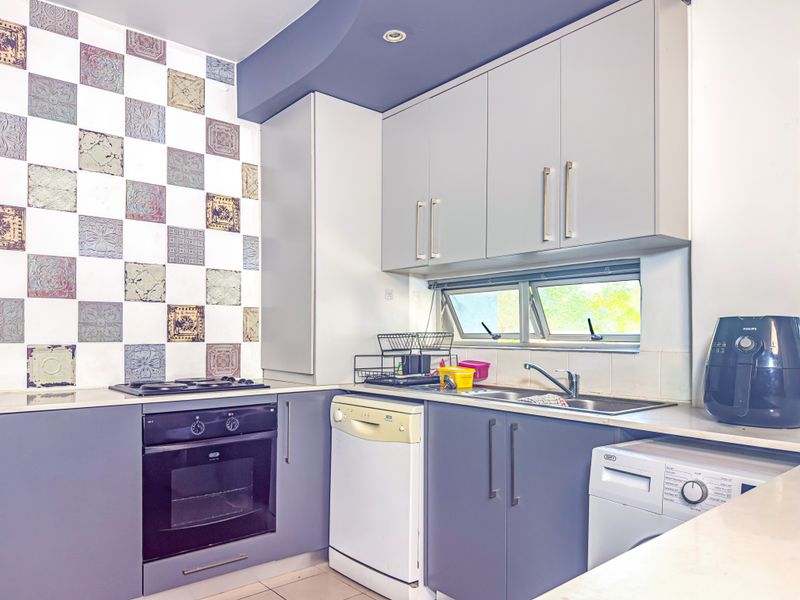A functional kitchen featuring modern grey cabinetry, a decorative tiled splashback, built-in oven, hob, and a stainless steel sink with window view.