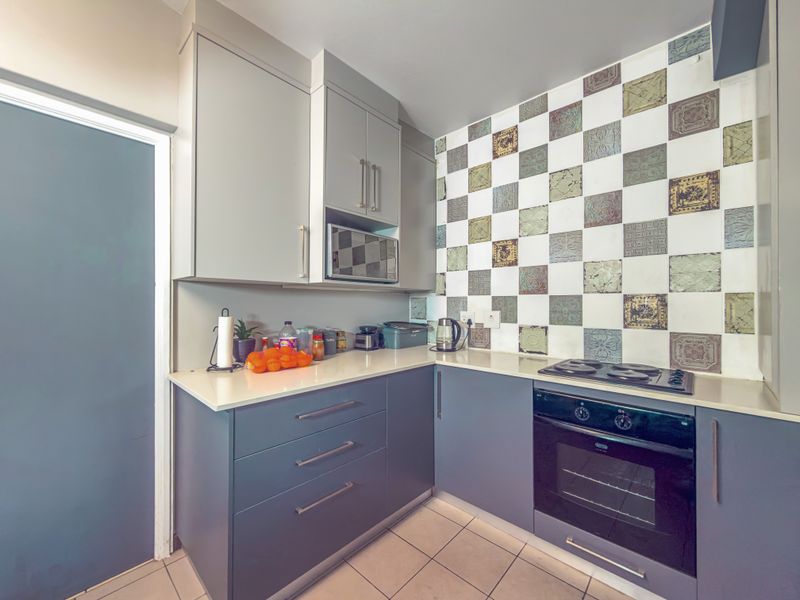 A compact kitchen featuring modern grey cabinetry, a built-in oven and hob, stone countertops, and a decorative tiled splashback.
