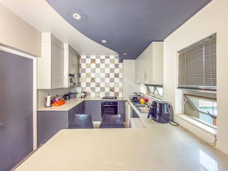 Modern kitchen featuring sleek cabinetry, stone countertops, a built-in oven and hob, and a decorative tiled backsplash with integrated lighting.