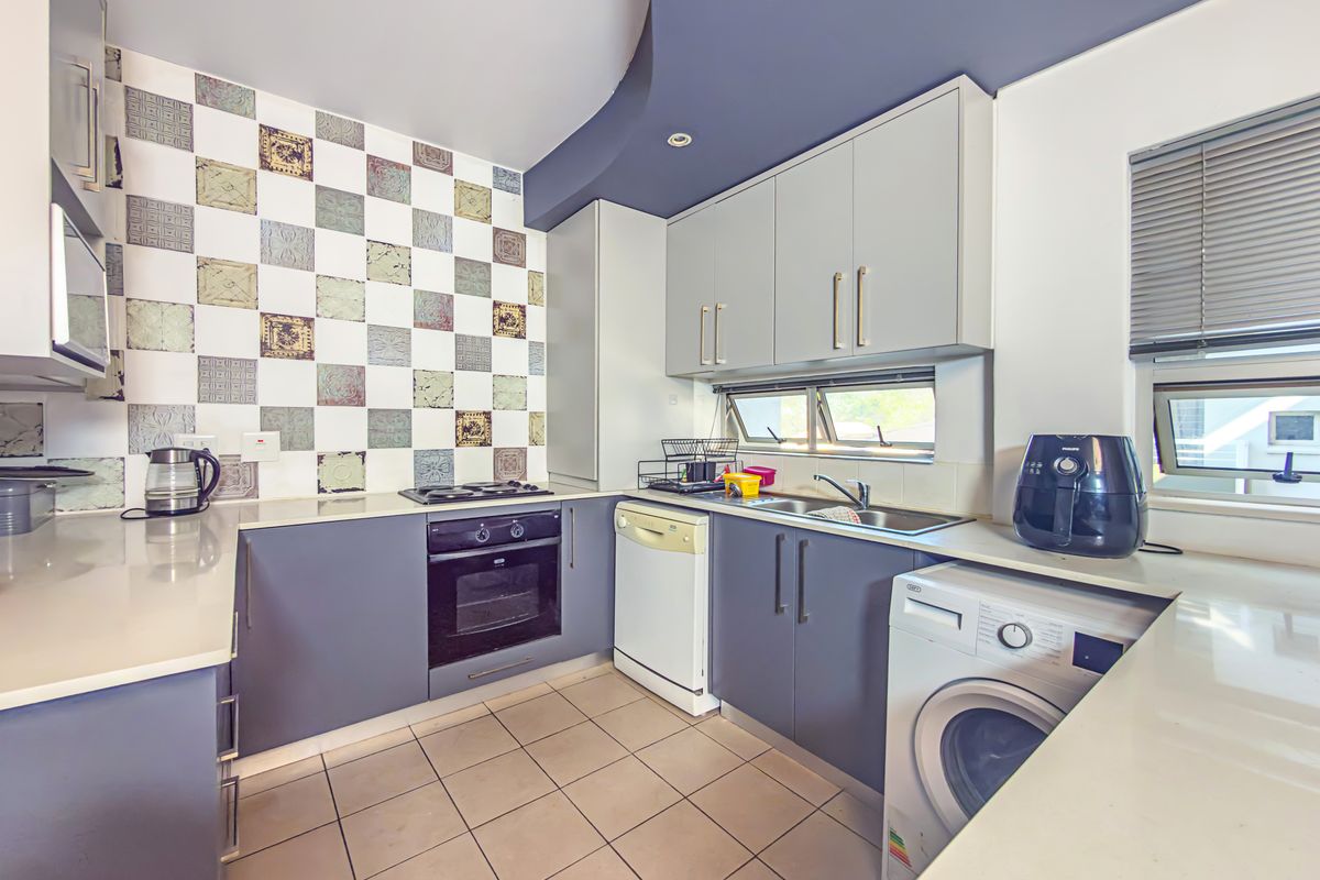 A functional kitchen featuring modern grey cabinetry, stone countertops, a built-in oven with gas hob, and unique decorative wall tiling.