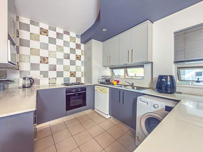 A functional kitchen featuring modern grey cabinetry, stone countertops, a built-in oven with gas hob, and unique decorative wall tiling.