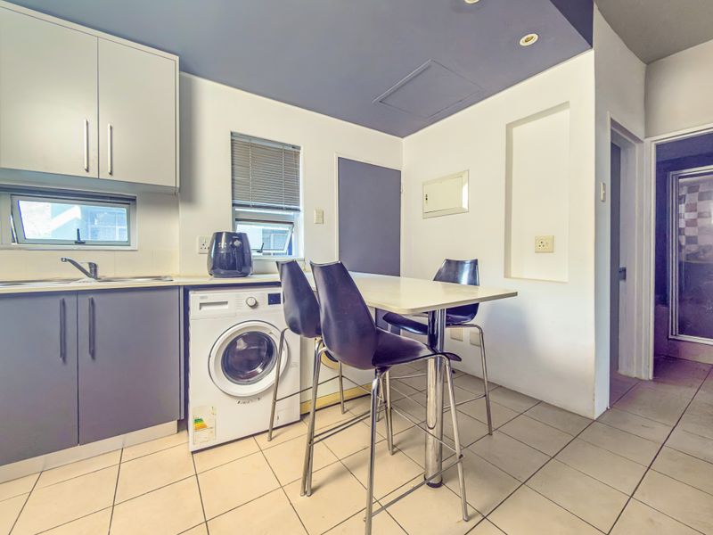 Compact kitchen featuring built-in cabinetry, tiled flooring, and a functional layout with integrated laundry plumbing and a breakfast bar area.