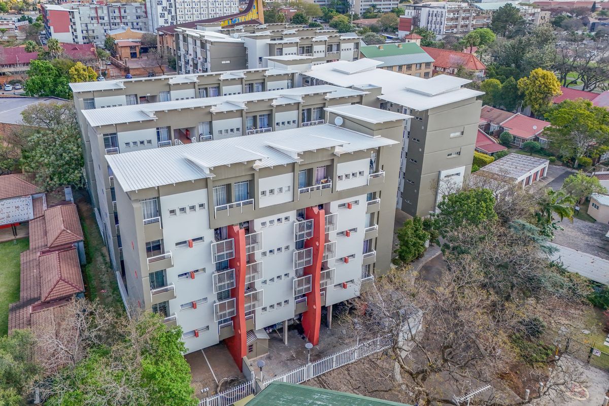 Aerial view of a multi-story apartment complex featuring modern architectural design, balconies, and surrounding paved grounds within an urban residential setting.