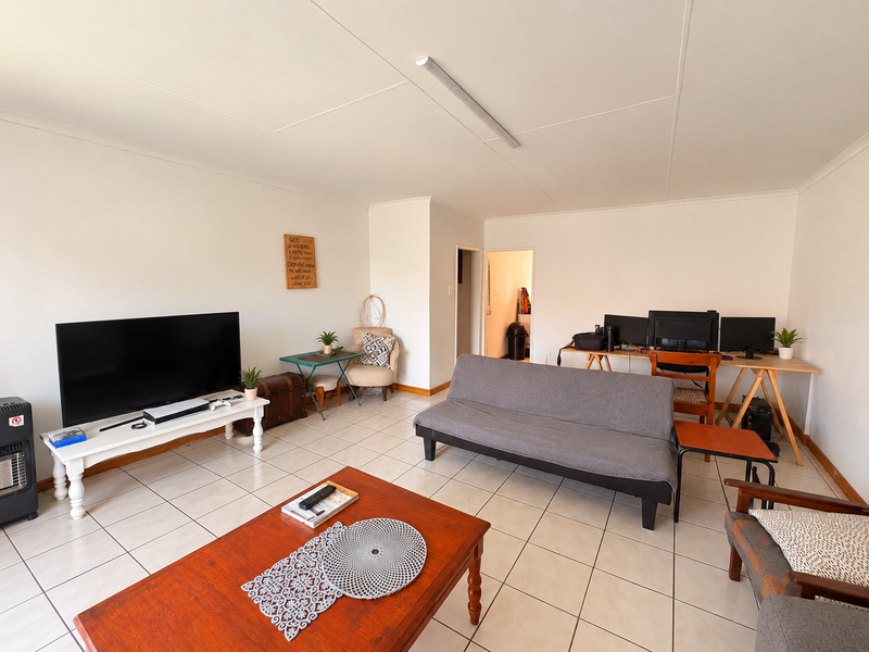 A spacious living room featuring neutral tiled flooring and simple overhead lighting, offering a versatile layout for comfortable daily living.