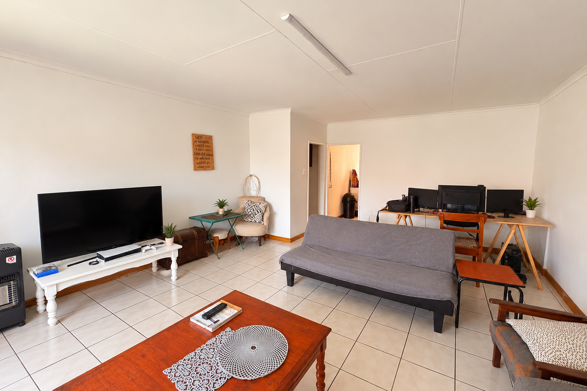A spacious living room featuring neutral tiled flooring and simple overhead lighting, offering a versatile layout for comfortable daily living.