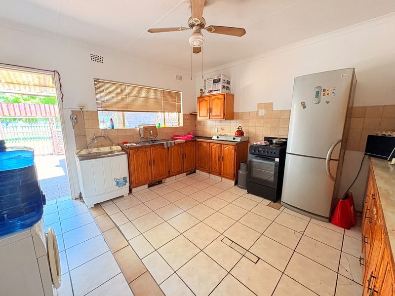 A functional kitchen featuring wooden cabinetry, tiled backsplash, and tiled flooring, with direct access to an outdoor area.