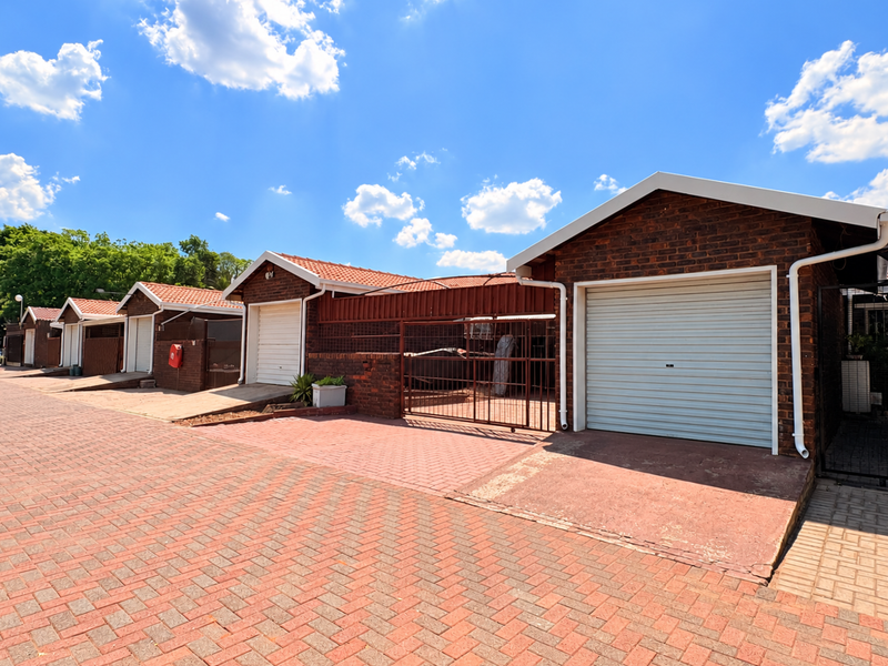 A row of brick-built townhouse garages featuring roller shutter doors and a paved driveway area under a clear blue sky.