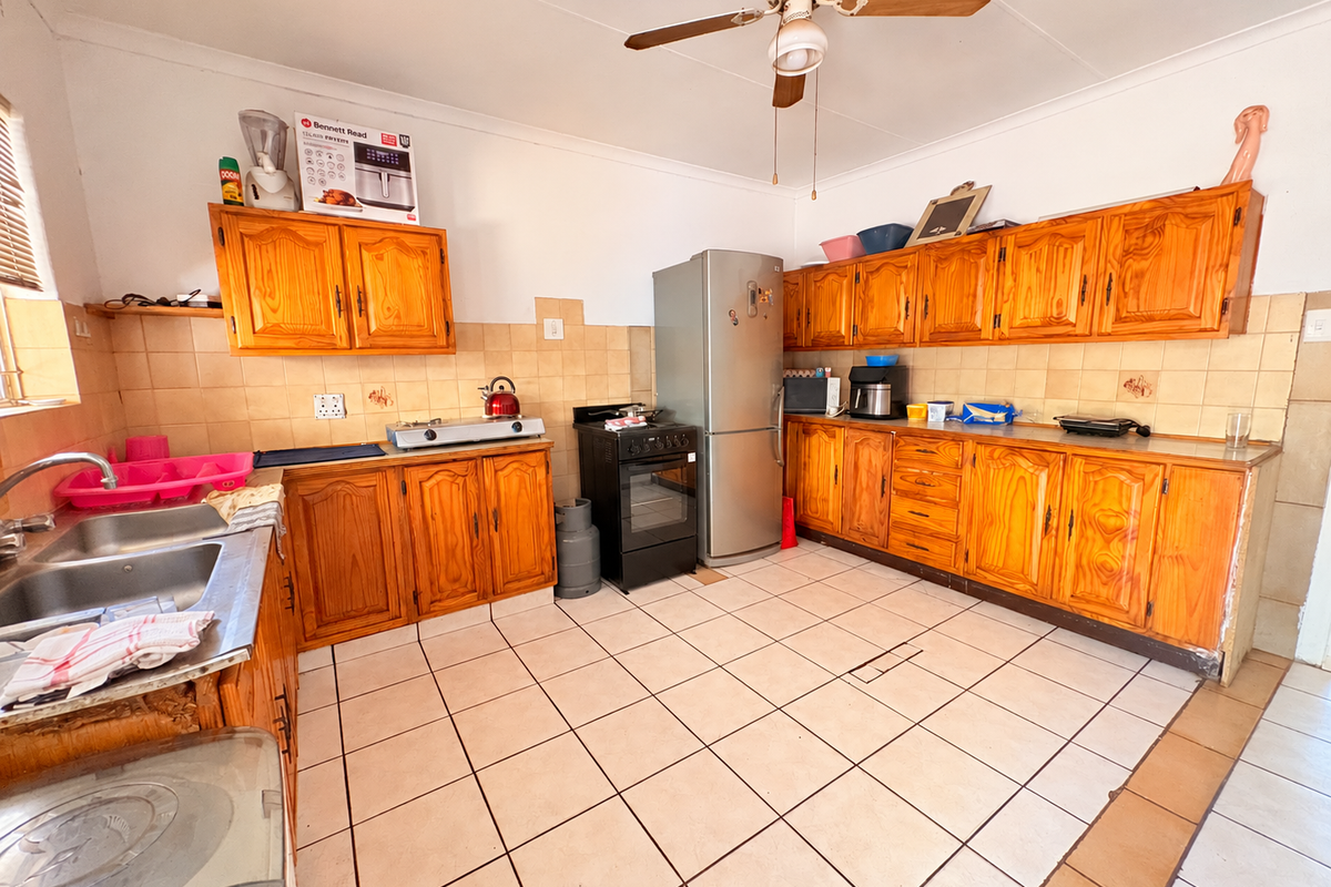 A dated kitchen featuring wooden cabinetry, tiled backsplash, and tiled flooring, offering a functional layout with potential for modern renovation.