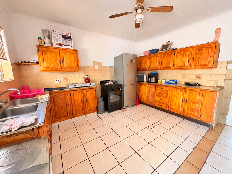 A dated kitchen featuring wooden cabinetry, tiled backsplash, and tiled flooring, offering a functional layout with potential for modern renovation.