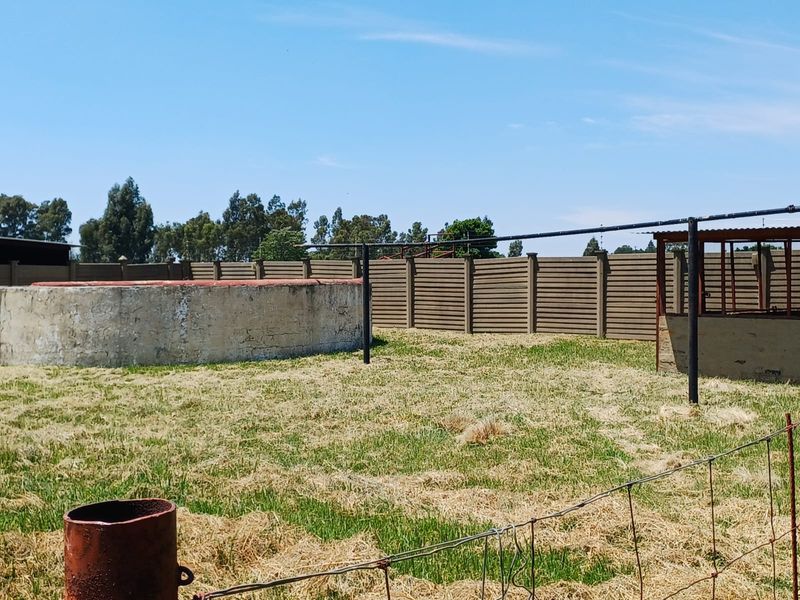 Outdoor garden area featuring a large concrete water reservoir, perimeter boundary walling, and basic wire fencing.