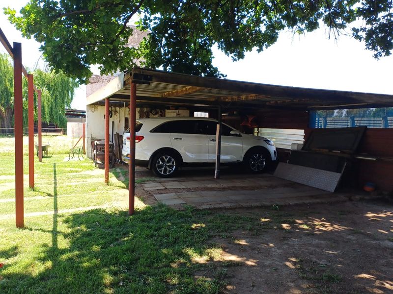 An open-sided carport structure with paved flooring and metal roofing, providing covered parking space.