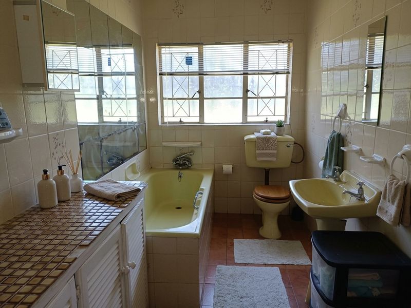 A dated bathroom featuring a yellow suite, tiled vanity countertop, and full wall tiling, offering significant potential for a modern renovation.