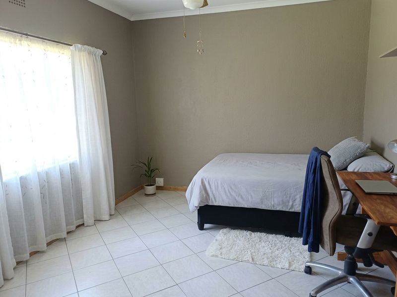 A functional bedroom featuring neutral wall tones, tiled flooring, and natural light through a large window.